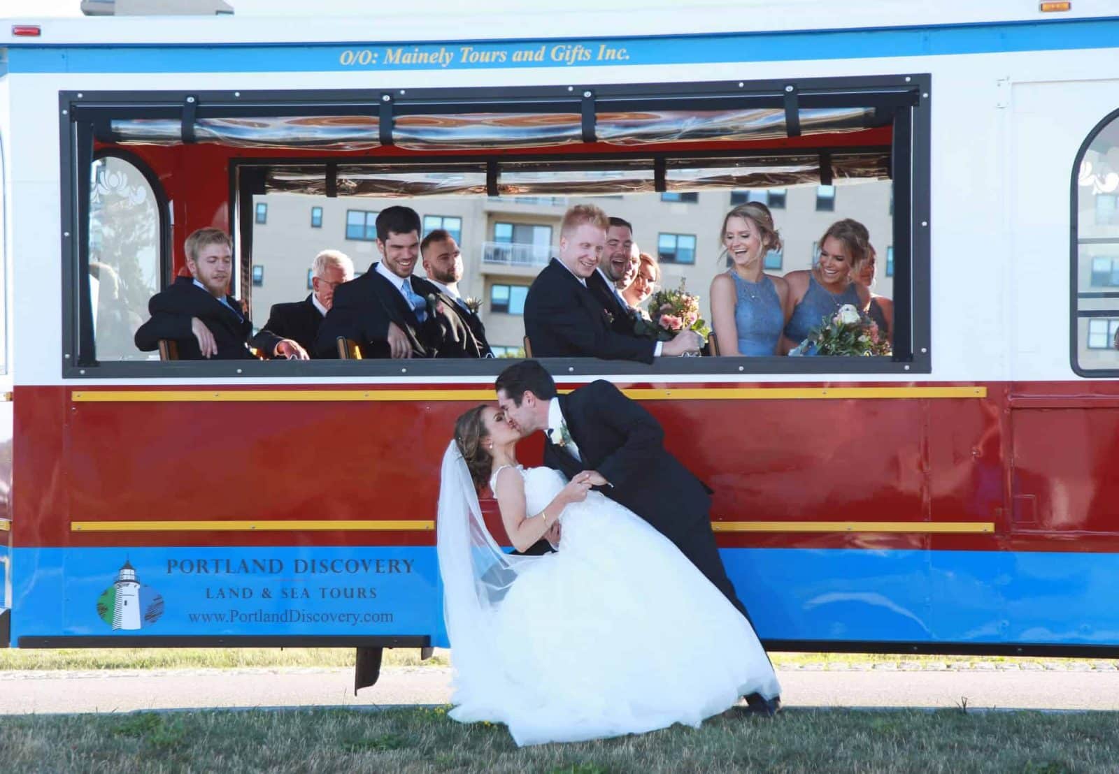 bride and groom kissing in front of trolley, bridal party watching from the inside