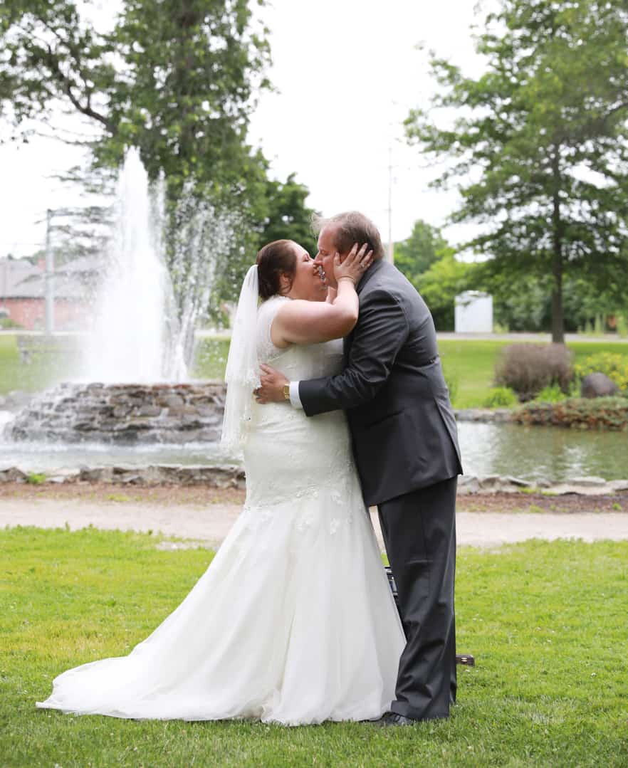 First kiss as bride and groom with park fountain behind them