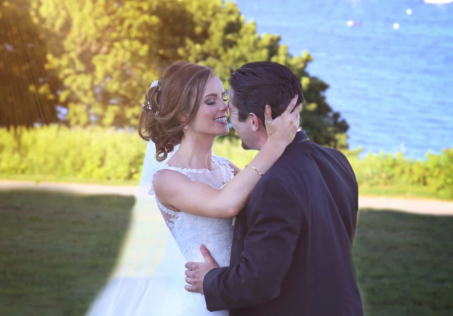 Bride and groom kissing near the ocean with sun beam in the left
