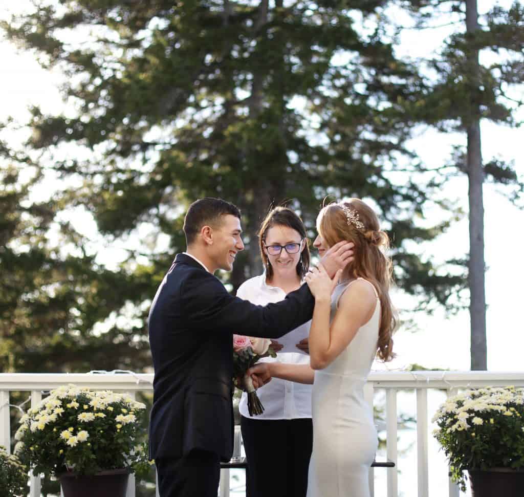 Bride and Groom on the porch getting married overlooking the ocean. Groom kindly touching the brides check 