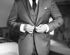 groom doing the buttons on his suit jacket in black and white