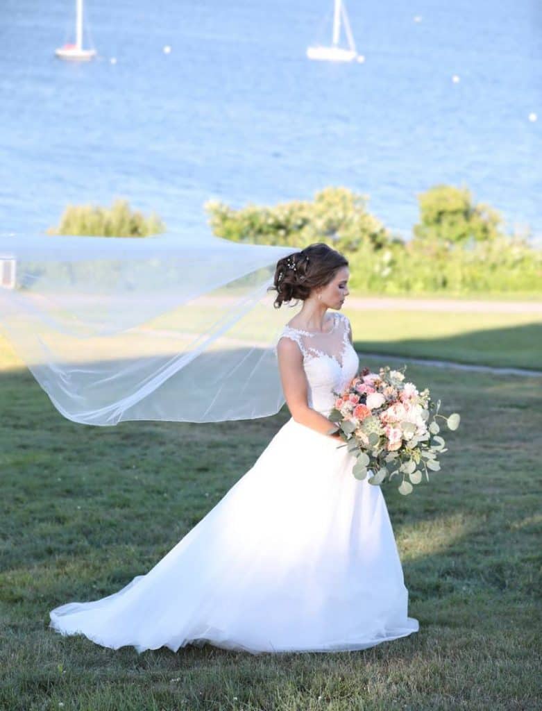 bride facing away from the camera holding bouquet near the ocean, boats in the background