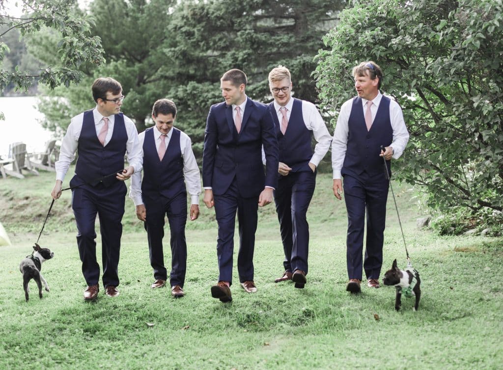 groom and groomsmen walking towards the camera with the two puppies