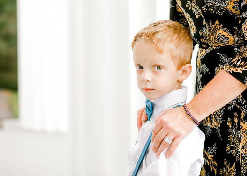 side profile of the ring bearer looking at the camera with his mothers hands on his shoulders