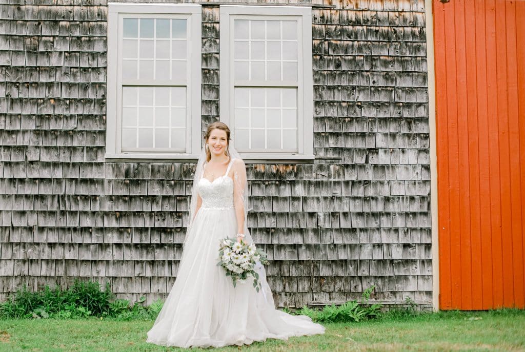 bride portrait looking at the camera with bouquet in front of a barn with a red side