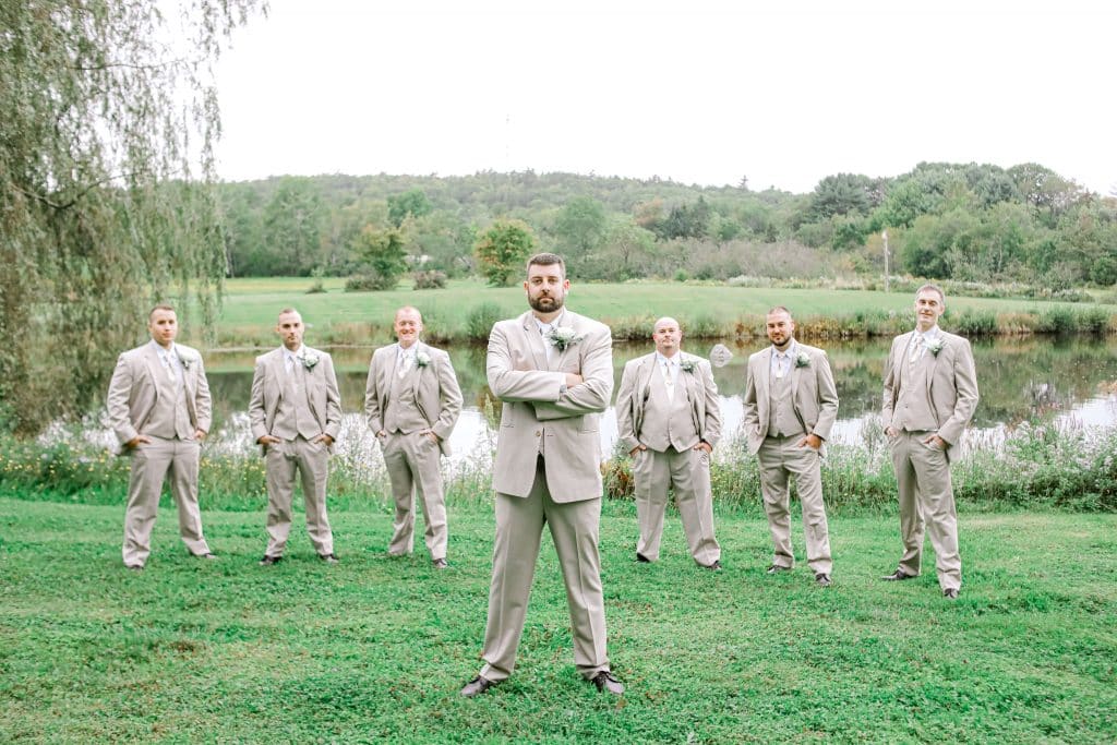 Groom and groomsmen standing near a lake looking at the camera with the groom in front as the main focus