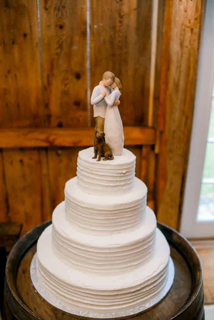 Maine Made wedding cake. White four tear cake with bride and groom figures on top with a rustic wood background