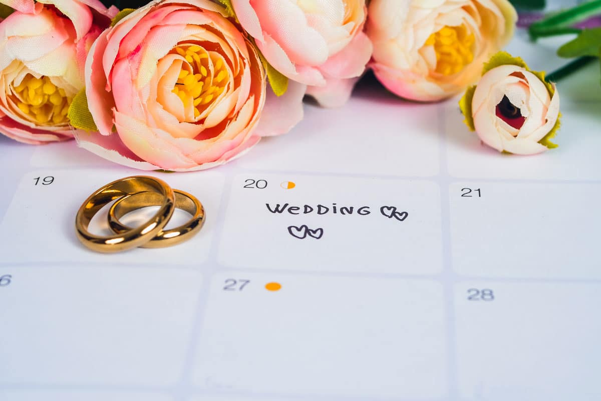 steps to planning your wedding, a calendar with real flowers sitting on top with wedding bands next to a wedding date annotated with hearts