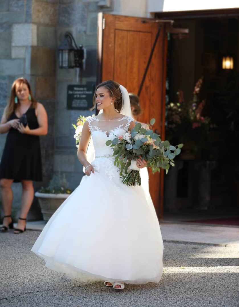 bride coming out as a wife, hand on hip, holding flowers outside of the church