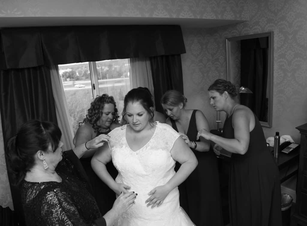 Bridesmaids helping the bride into her dress photo in black and white.