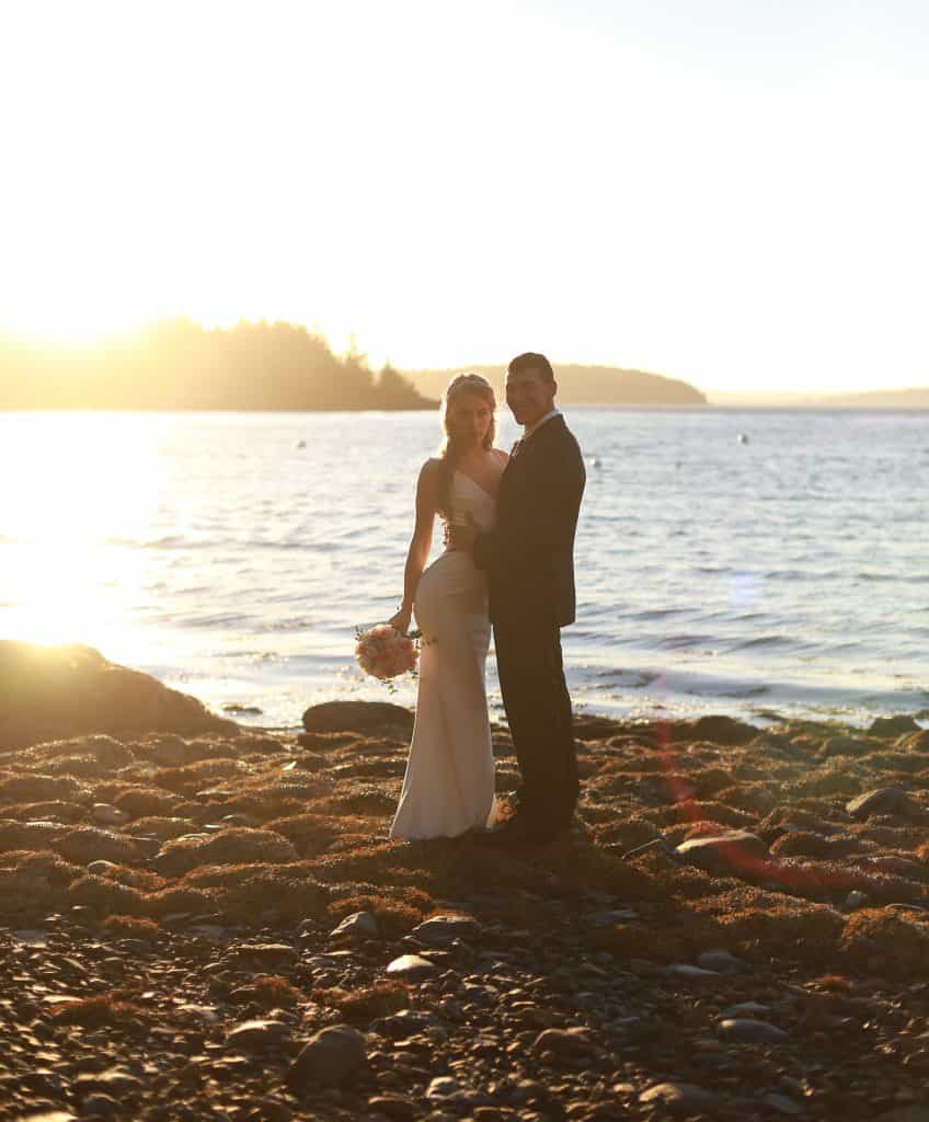 bride and groom at their bar harbor wedding on the ocean at sunset looking at the camera hugging