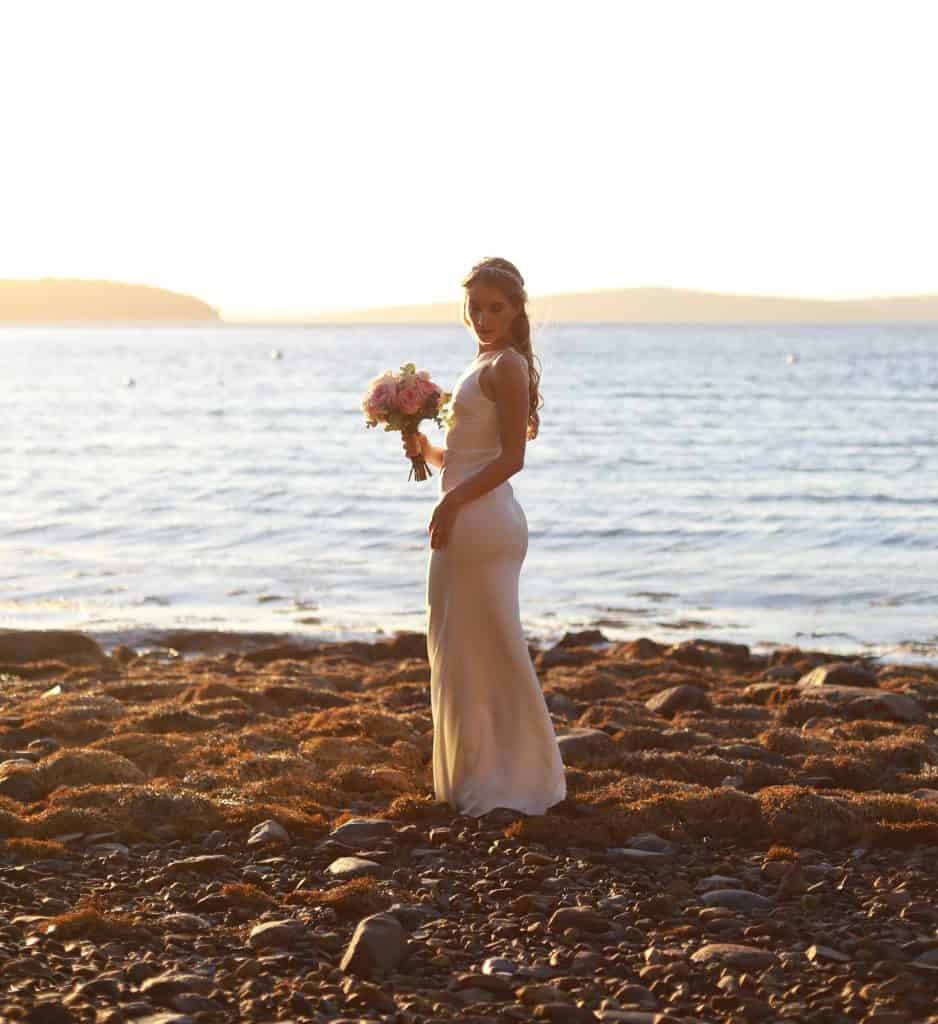 Bride facing the ocean overlooking her shoulder to the camera on the beach