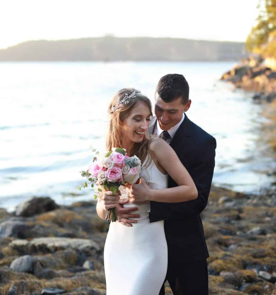 Bride and groom embraced in a hug on the beach overlooking the ocean