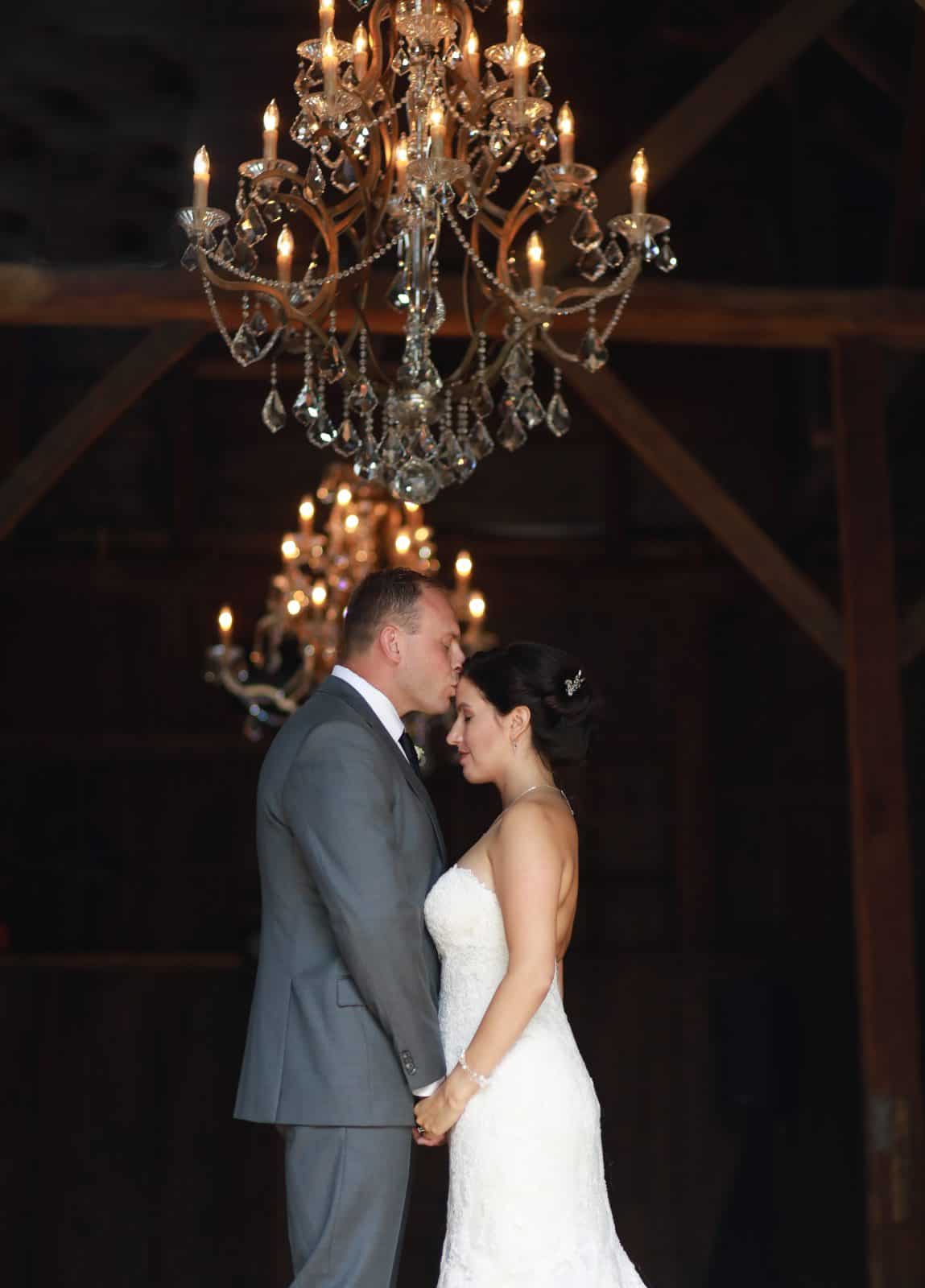 Bride and Groom in a barn with a chandelier embracing one another