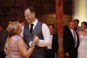 bride and groom dancing with their parents in the barn with a chandelier