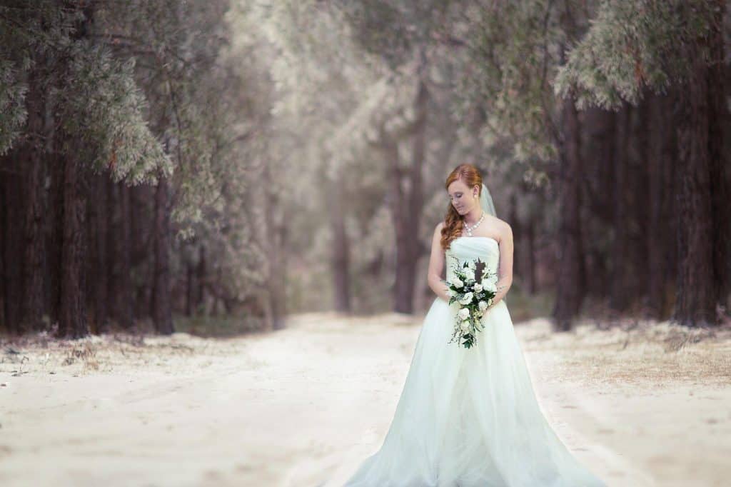 bride in winter wonderland surrounded by trees, holding bouquet looking down her right shoulder