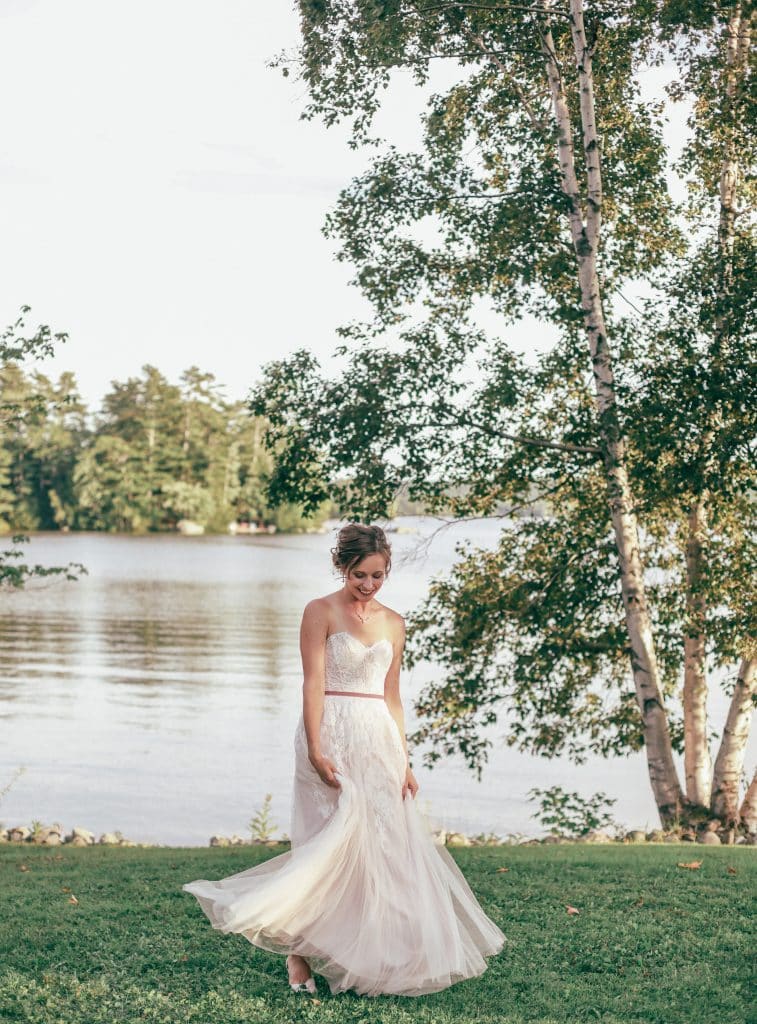 bride dancing in her wedding gown looking down near the lake holding her bouqet