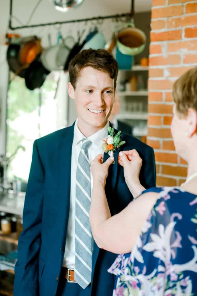 groom in the barn kitchen with his mother pinning on his boutineer