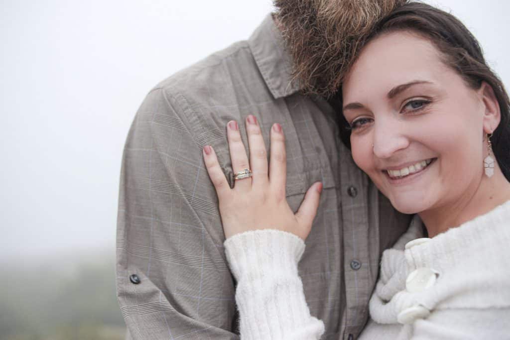 newley engaged woman looking at the camera, hand on her fiances chest