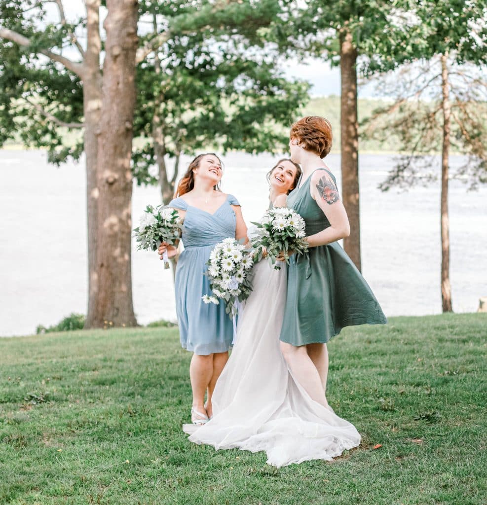 Bride and her bridesmaids laughing candidly, river behind them