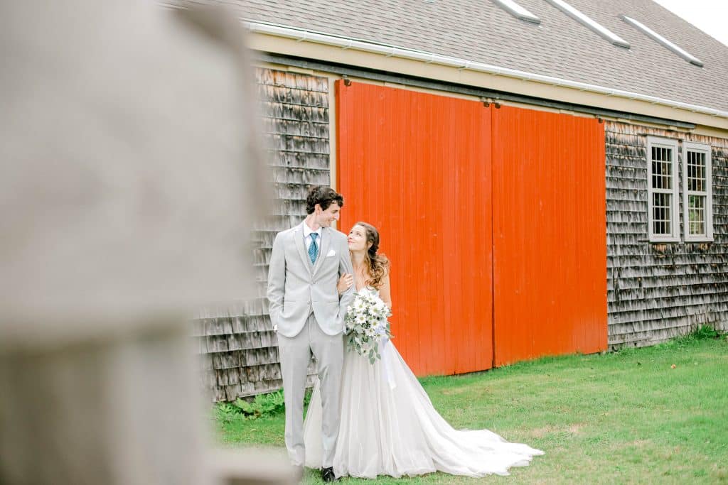 bride and groom looking at each other in front of a red barm