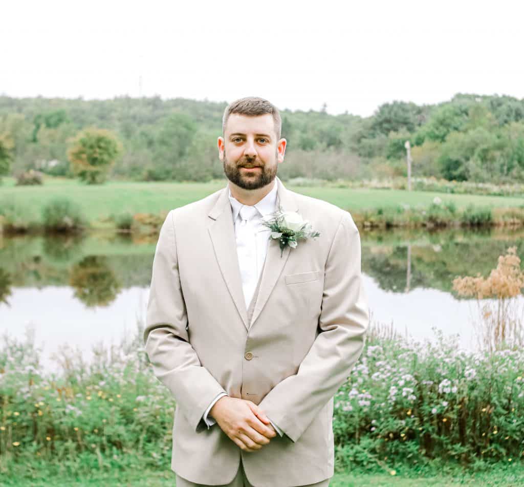 Groom looking at the camera near a lake outside