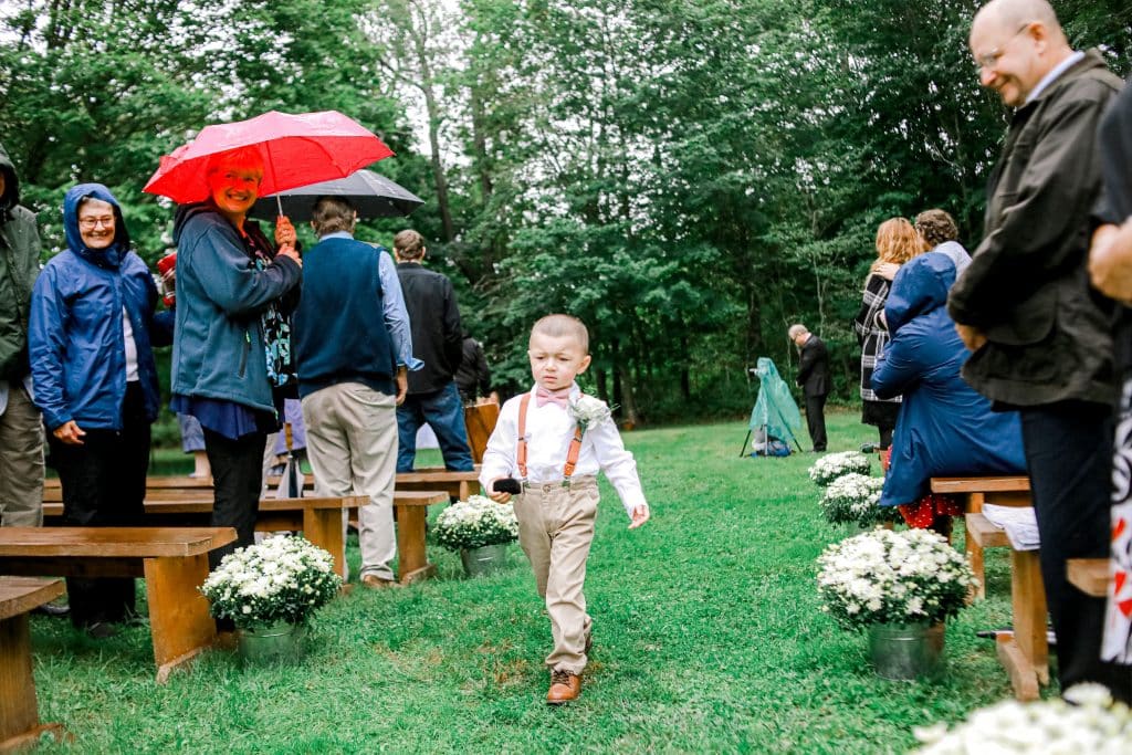 four tear white wedding cake on rustic background and ring bearer walking down the isle with the rings