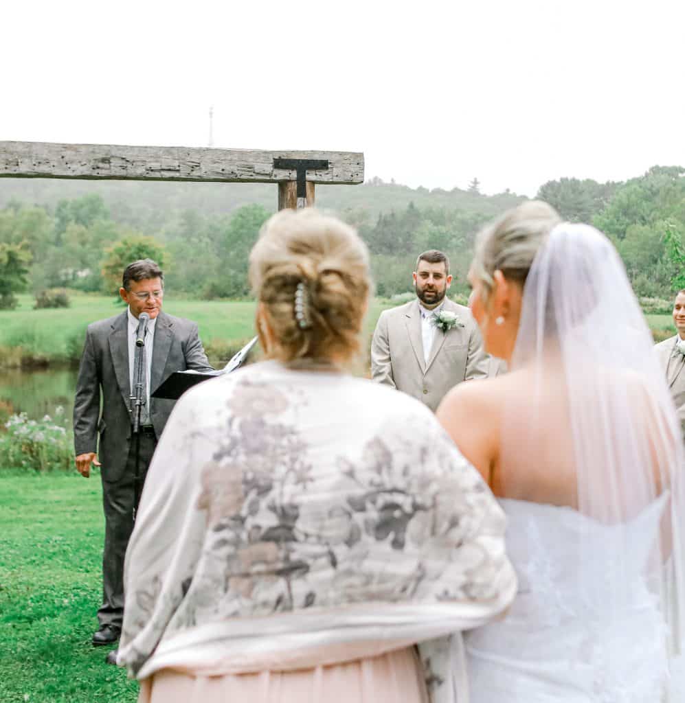 Mother walking daughter down the isle, grooms reaction through their arms.