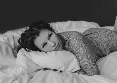 bride laying on her stomach hugging a pillow looking at the camera, black and white