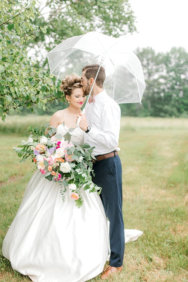 southern Maine wedding photographer captures bride and groom holding flower bouquet and clear umbrella