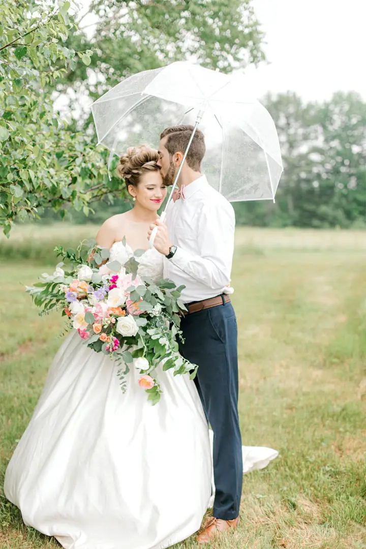bride and groom holding flower bouquet and clear umbrella