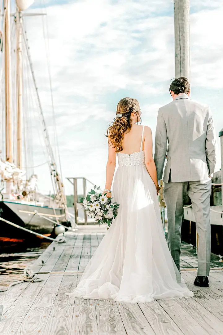 bride and groom walking along a dock next to a sailboat in maine