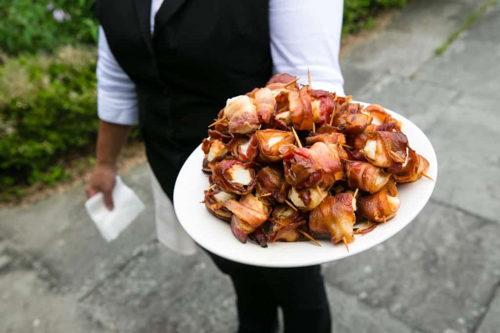 a server holding a plate of bacon wrapped scallops