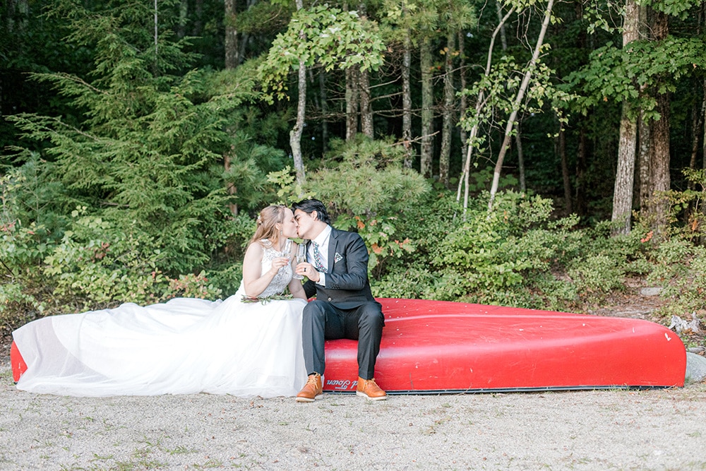 bride4 and groom sitting on a red canoe on a sandy beach with forest behind them