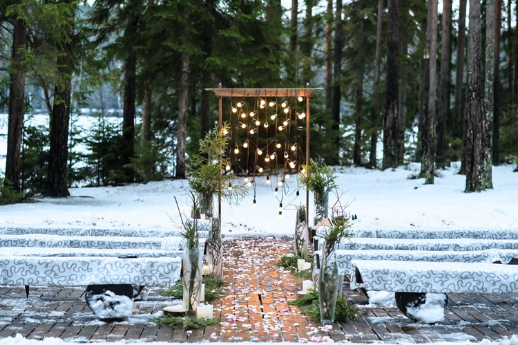 winter wedding in maine with snow on the ground, pine trees in the background, and and an arch with sparkling lights
