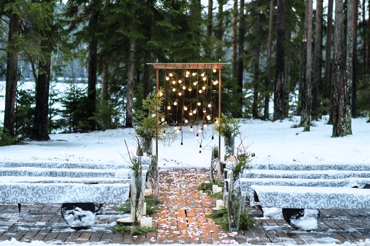 winter-wedding-in-maine winter wedding in maine with snow on the ground, pine trees in the background, and and an arch with sparkling lights