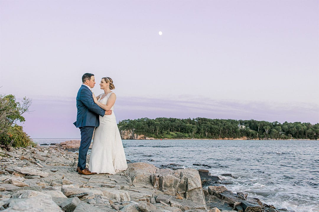 destination wedding in maine inn on peaks island couple portrait in front of rock beach and island in the background