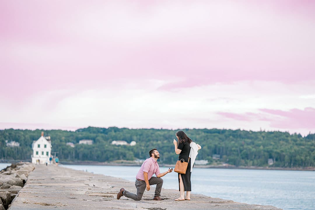 a man down on one knee surprising his girlfriend with a proposal on Rockland's Breakwater