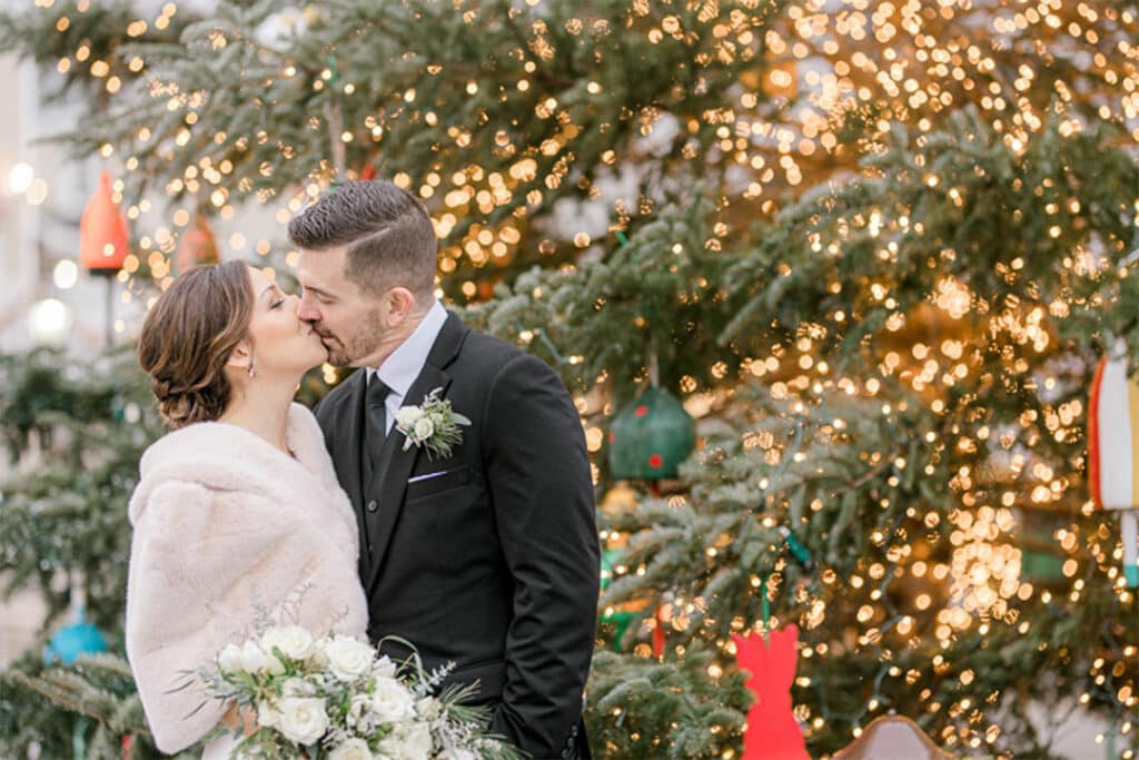 bride and groom kissing next to large christmas tree