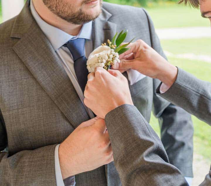 Close-up of groom's boutonniere being adjusted.