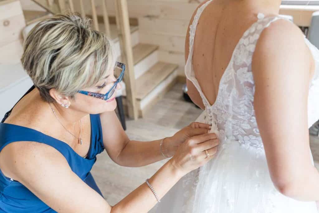 Close-up of bride's mother buttoning up her wedding dress